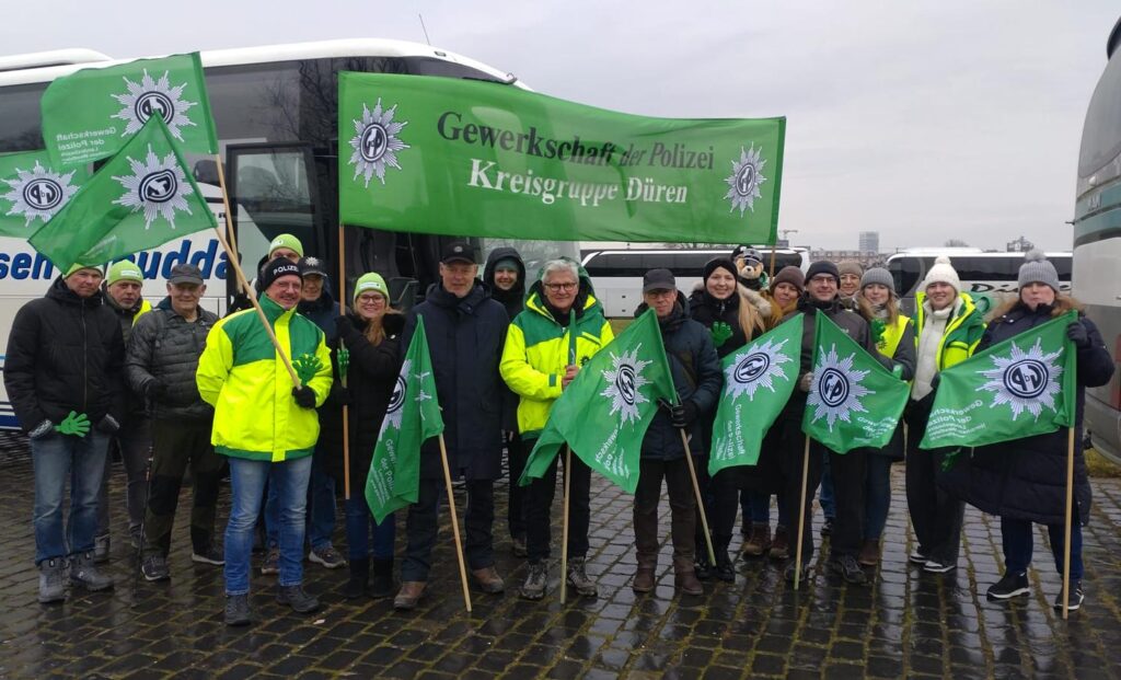 Eine Gruppe von Menschen steht mit einem grünen Banner und grünen Fahnen der GdP vor einem Bus