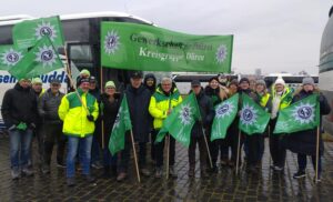 Eine Gruppe von Menschen steht mit einem grünen Banner und grünen Fahnen der GdP vor einem Bus
