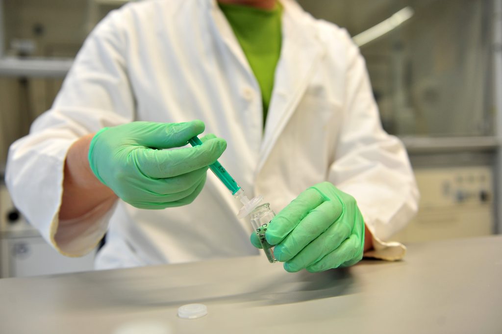 Beschäftigte im Labor im weißen Kittel hantiert mit Pipette und Reagenzglas