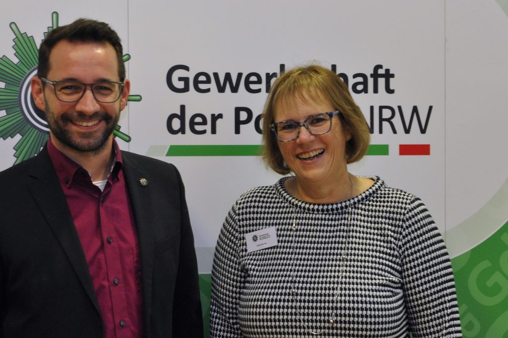 Rene Klemmer und Jutta Jakobs stehen beim Tarifforum vor einem Plakat der Gewerkschaft der Polizei und lachen in die Kamera