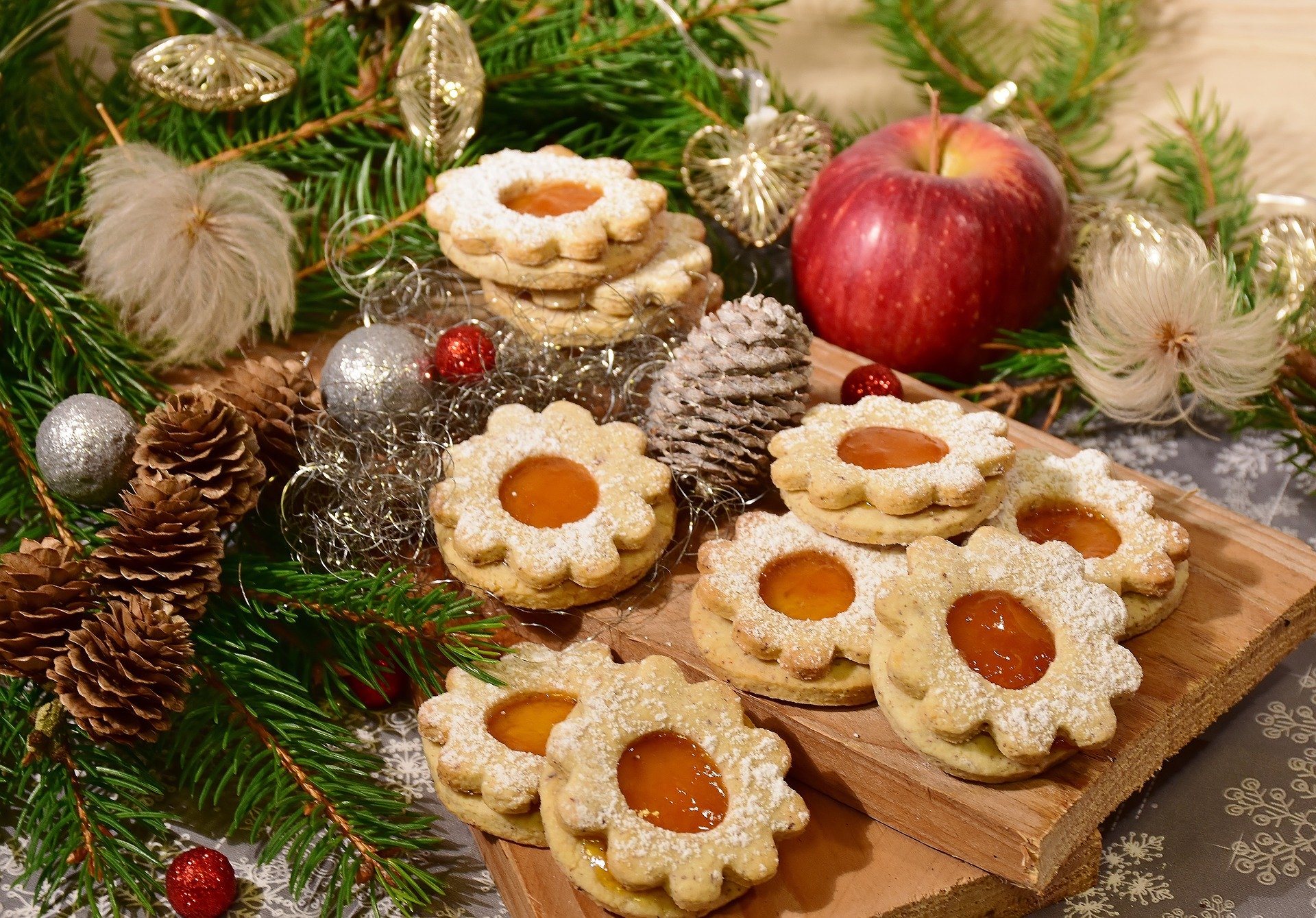 Weihnachtsplätzchen nett dekoriert auf einem Brett zwischen Tannenzweigen, tannenzapfen und einem Apfel